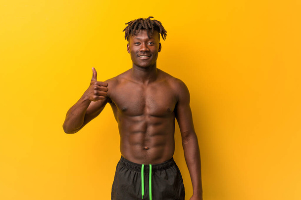 Young black man shirtless wearing swimsuit smiling and raising thumb up - Photo, Image