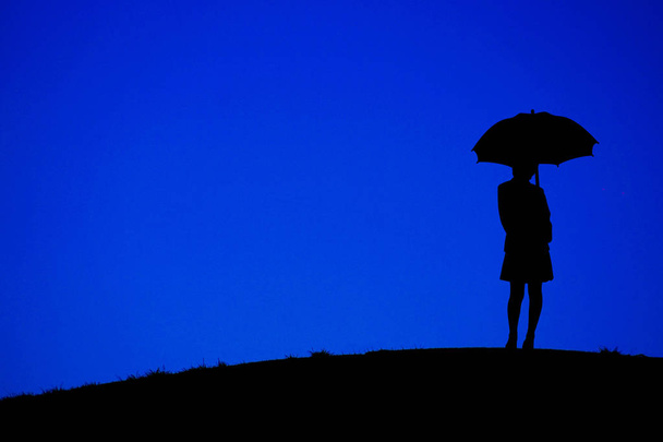 Tepelerin olduğu gece elinde şemsiye tutan kadın. - Fotoğraf, Görsel