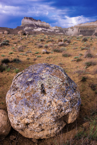 Большой камень, покрытый лишайником в степи, рядом с высокими скалами
 - Фото, изображение