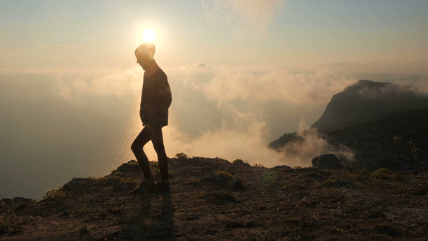 Silhouette einer jungen Frau, die an einer Klippe über einem Meer entlang geht und von einem hohen Berg auf der Krim einen wunderschönen dramatischen Sonnenuntergang beobachtet. - Filmmaterial, Video