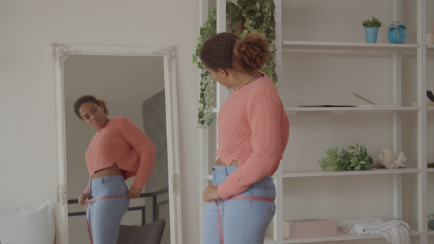Lovely positive female measuring her hips indoors - Filmati, video
