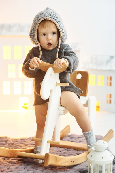 A little child sits on a wooden skate on background of a toy hou - Fotoğraf, Görsel