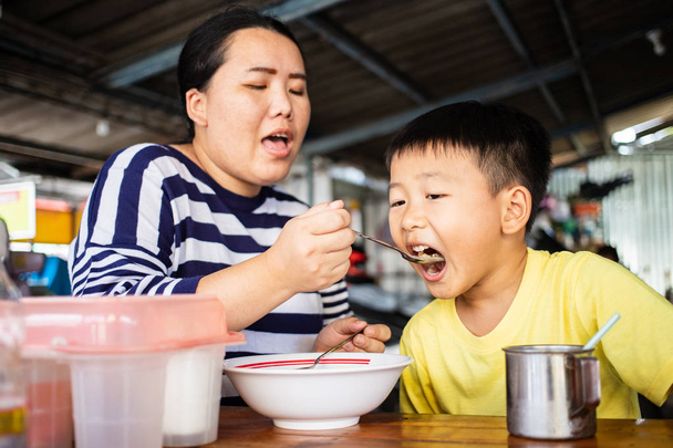 Mère asiatique nourrissant son fils dans un magasin de nouilles
 - Photo, image