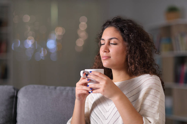 Relaxed woman smelling coffee cup in the night - Fotoğraf, Görsel
