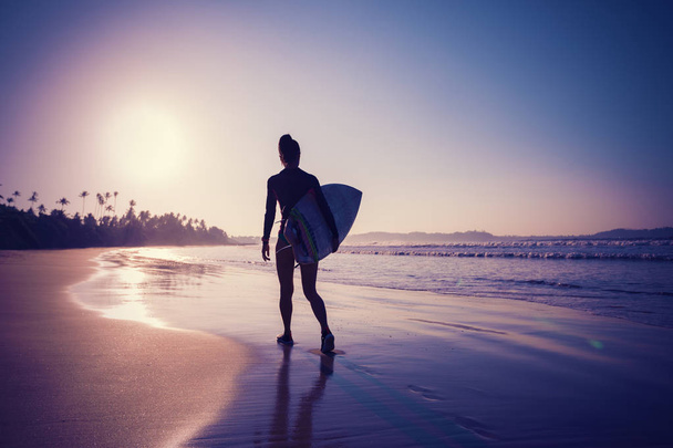 Fit female surfer with surfboard ready to surf on sunrise beach - 写真・画像