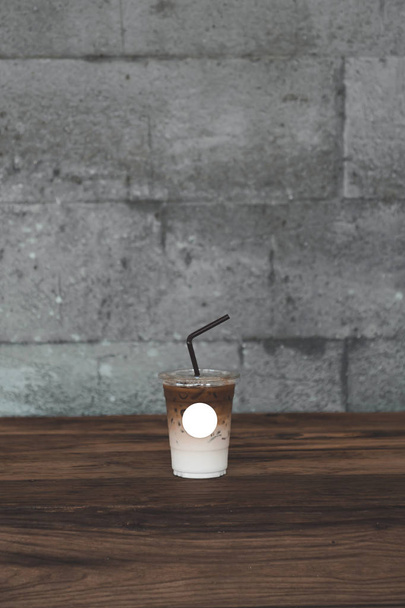 Ice Coffee on take away cup with Empty label για εισαγωγή λογότυπου και template.Κύπελλο καφέ σε ξύλινο τραπέζι και grunge σκυρόδεμα φόντο. - Φωτογραφία, εικόνα