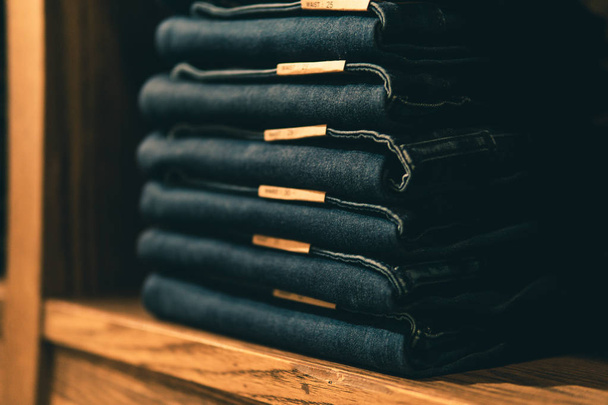 Pantalones vaqueros apilados con varios tamaños de cintura en estantes o armarios y enfoque selectivo
. - Foto, Imagen