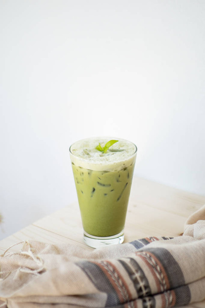 Παγωμένο πράσινο τσάι ή matcha latte σε λευκό ξύλινο τραπέζι και ρούχα διακόσμηση αντικείμενο. - Φωτογραφία, εικόνα