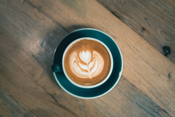 Κύπελλο του καφέ με latte τέχνη σερβίρεται σε ξύλινο τραπέζι.Flat Lay φλιτζάνι καφέ. - Φωτογραφία, εικόνα