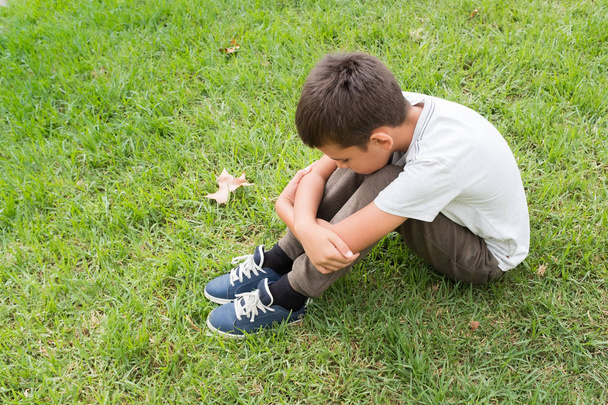 Дитина сидить на траві з підборіддям відпочиває на колінах, концепціях самотності і смутку
. - Фото, зображення