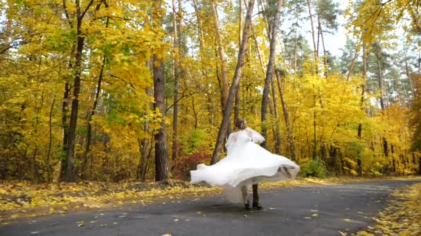 スローモーション。新郎は、紅葉の木々の間でゆっくりと動きながら、秋の森の中で花嫁を回転させます。若い魅力的な幸せな愛する新婚旅行のダンスと公園でスピン. - 映像、動画