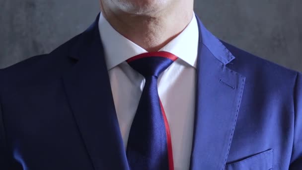 arms of person in blue suit straightens necktie on neck on background of gray concrete wall - Materiał filmowy, wideo