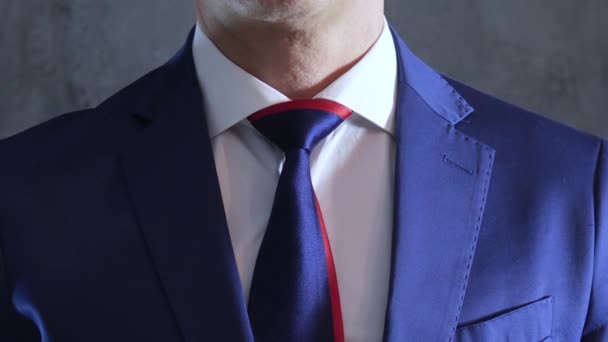 üzleti ember szmokingban egyenesíti nyakkendő a torok hátterében szürke beton fal - Felvétel, videó