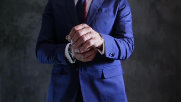 elegantní módní oblek muže, který opravuje rukávy, zásnubní prsten a náramkové hodinky na pažích proti šedé stěně - Záběry, video