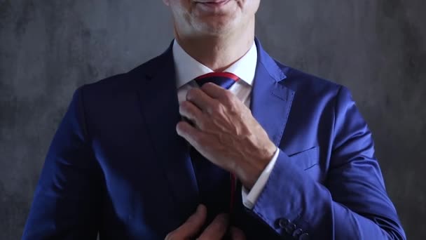 stylowy człowiek korygujący krawat na szyi na tle szarej ściany betonowej - Materiał filmowy, wideo