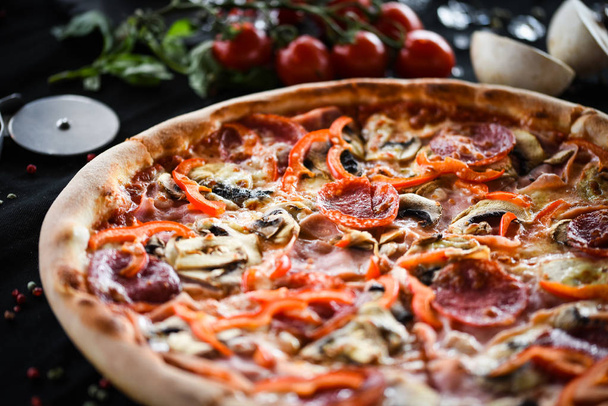ízletes olasz pizza capriciosa friss összetevőkkel - zöldségek, sajt, sonka, paradicsom szósz és bazsalikom - Fotó, kép
