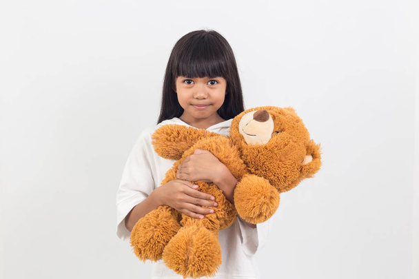 asian little girl is hugging a teddy bear on a white background - Фото, изображение