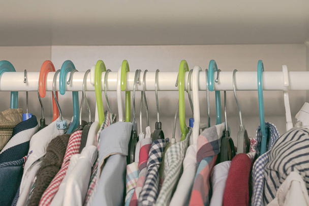 színes vállfák és gyermekruhák egy ruhaszárítón lógnak a szekrényben. - Fotó, kép