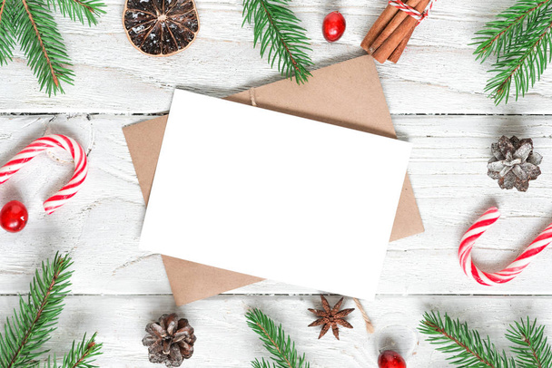 Χριστουγεννιάτικη ευχετήρια κάρτα mock up σε πλαίσιο από κλαδιά ελάτης, διακοσμήσεις, μούρα, καραμέλα και κουκουνάρια. επίπεδη ωοτοκία - Φωτογραφία, εικόνα