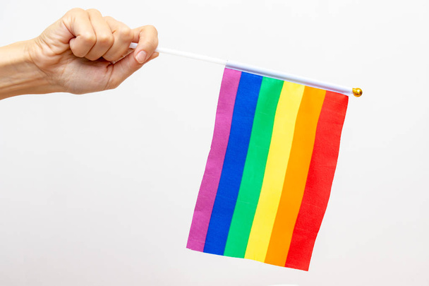A hand holding an lgbt rainbow flag as a symbol of tolerance and protection of gay rights, white background, copy space - Фото, зображення
