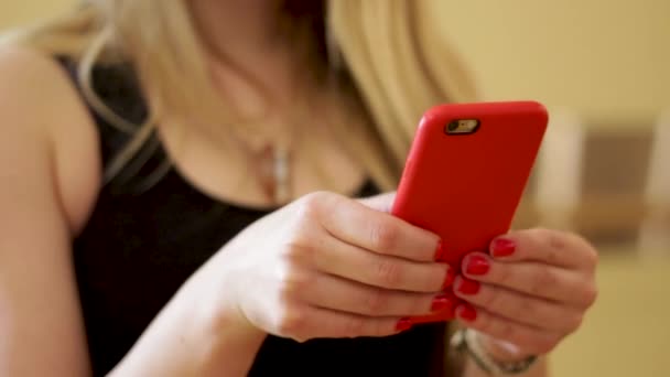 Blondýny žena s červenými nehty texty na telefonu s červeným pouzdrem - Záběry, video