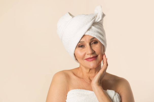stylish beautiful aged woman in a white towel on a beige background - Фото, изображение