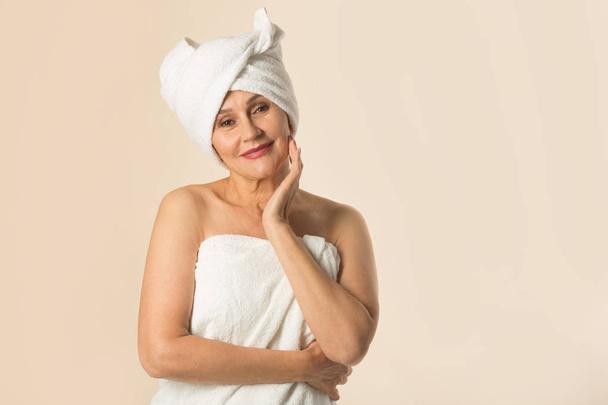 stylish beautiful aged woman in a white towel on a beige background - Zdjęcie, obraz