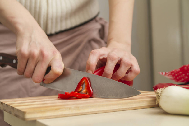 Couper du paprika rouge sur une planche à découper en bambou dans une cuisine, gros plan, personne
 - Photo, image