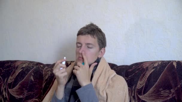 close up caucasian sick man sits on sofa and uses nasal spray for cold during illness wrapped in blanket - Video, Çekim
