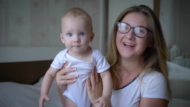 happy family, merry mother in glasses holds infant on hands and looks on camera close up in room - Footage, Video