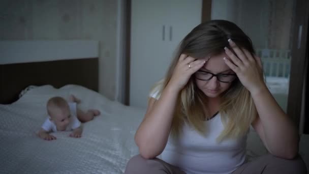 mujer cansada de niño, infeliz nerviosa joven madre sostiene la cabeza en el fondo niño acostado en la cama
 - Imágenes, Vídeo