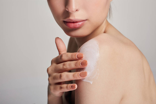 A young girl with clean fresh skin smears a body cream on her shoulder. Dry skin care. Beauty and care concept. - Foto, afbeelding