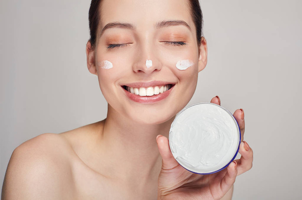 Close up beauty portrait of a laughing beautiful half naked woman with eyes closed holds in hand face cream. - Foto, imagen