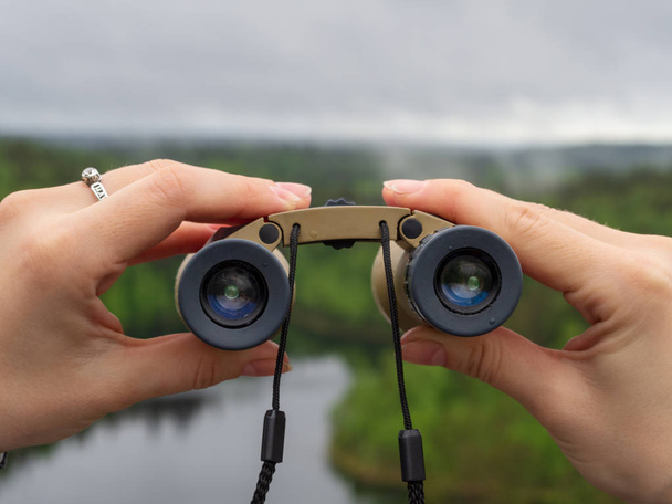 woman looks through binoculars. tourist girl on a rock in a forest near a lake - 写真・画像