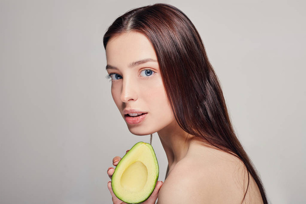 sexy brown-haired nude lady with perfect pure shine skin with avocado in the hand looking straight - Photo, image