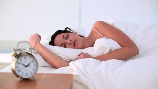Brunette being woken by her alarm clock in bed - Materiał filmowy, wideo