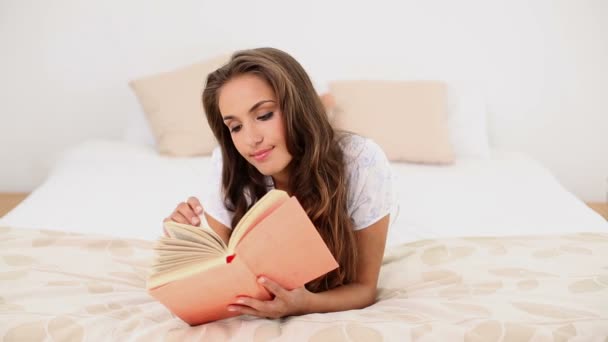 Young woman reading a book lying on her bed - Záběry, video
