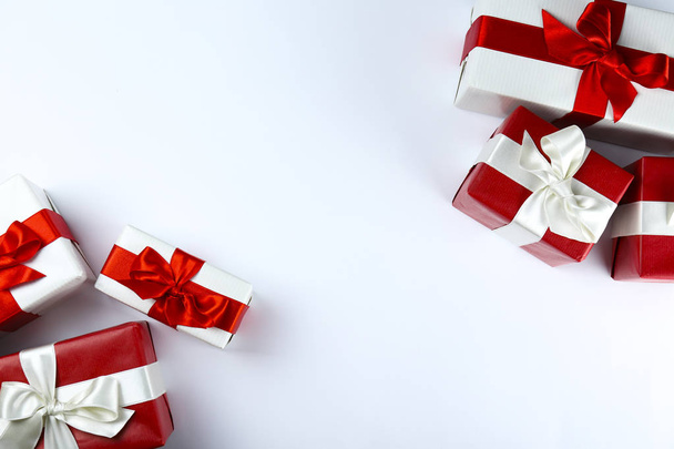 Ramo de regalos de Navidad envueltos en papel rojo y blanco atado con lazo de seda brillante. Múltiples regalos de año nuevo en envoltura roja y blanca. Vista superior, primer plano, espacio para copiar, fondo, plano
. - Foto, Imagen