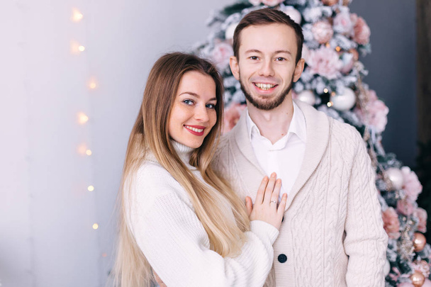ζευγάρι ερωτευμένο με λευκά πλεκτά πουλόβερ στο πίσω μέρος του χριστουγεννιάτικου δέντρου - Φωτογραφία, εικόνα