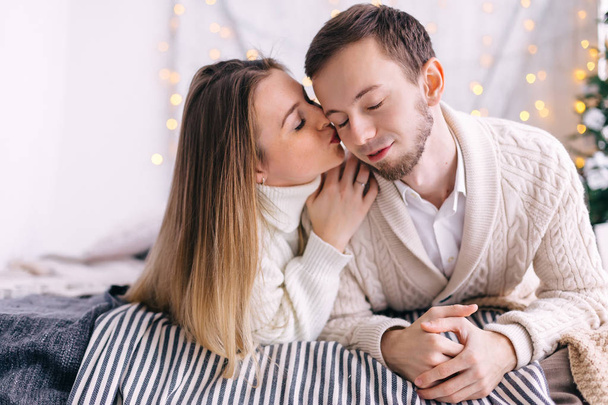 couple in white knitted sweaters lie on the bed and kiss. christ - Foto, Bild