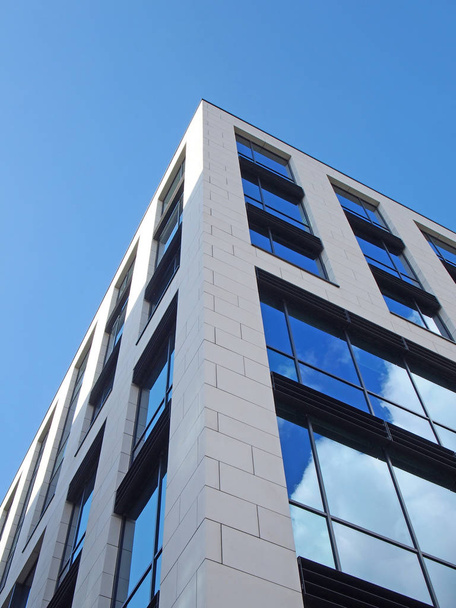 Mavi gökyüzü ve büyük cam pencerelere yansıyan bulutlarla beyaz, modern ofis binasının köşesine doğru. - Fotoğraf, Görsel