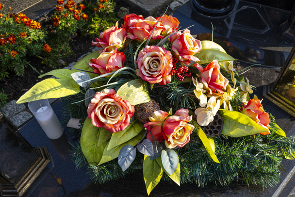Mesterséges virágok és gyertyák fekszenek a sírkövön a temetőben.. - Fotó, kép