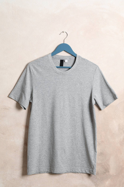 Hanger with blank gray t-shirt on light brown background, space  - Φωτογραφία, εικόνα