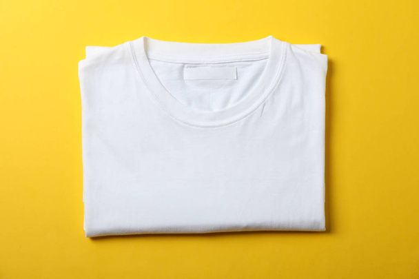 Folded blank white t-shirt on yellow background, space for text - Photo, Image