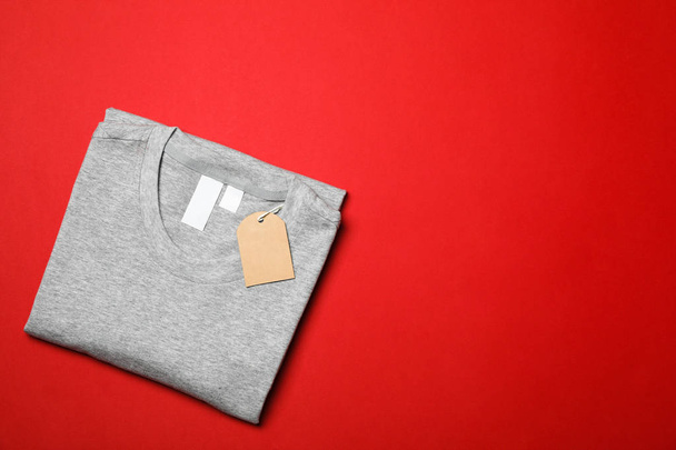 Folded blank grey t-shirt with tag on red background, space for  - Zdjęcie, obraz