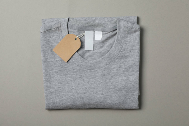 Folded blank gray t-shirt with tag on gray background, space for - Foto, Bild