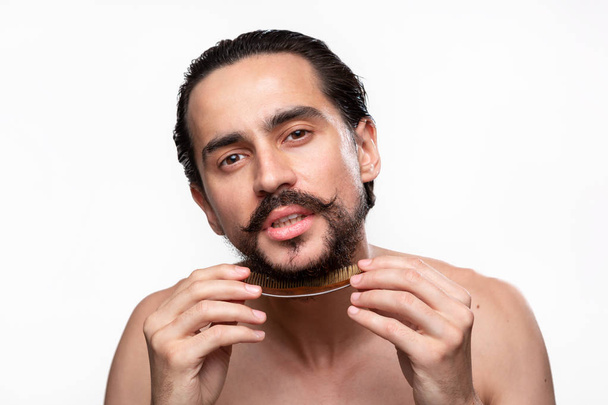Stylish handsome bearded with mustaches brushing his beard isolated over white background. Concept of morning treatment. - Foto, afbeelding