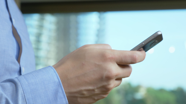 Közelkép. férfi kéz használja a telefont a háttérben egy ablak, ahonnan felhőkarcolók láthatók - Felvétel, videó