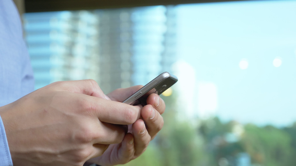 detailní záběr. mužské ruce používají telefon na pozadí okna, ze kterého jsou viditelné mrakodrapy - Záběry, video