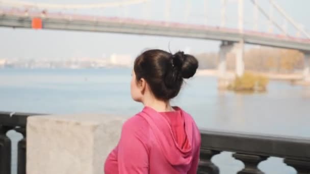 Close up view of young chubby female doing nordic walking along city river with bridge on background. Weight loss concept - Filmati, video